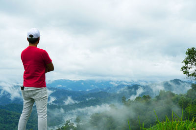 Rear view of man standing on mountain against sky