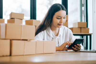 Young woman using mobile phone while sitting in box