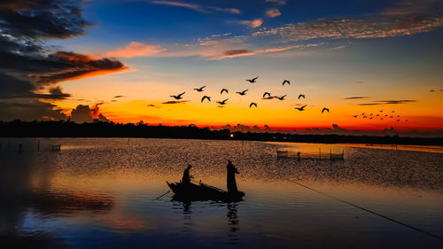 Silhouette birds flying over lake against sky during sunset