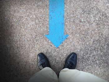 Low section of man standing by blue arrow symbol on footpath
