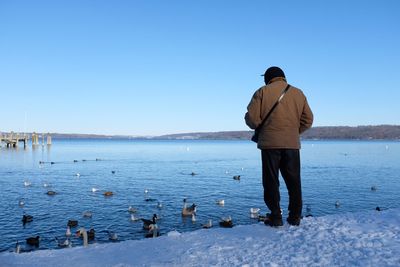 Rear view of man standing by sea against clear sky