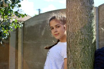 Portrait of smiling woman standing by tree trunk