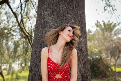 Mid adult woman tossing hair against tree trunk in park