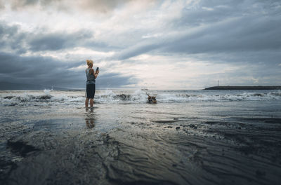 A woman playing with the dogs on beach against sky