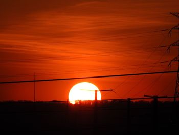 Silhouette electricity pylon against orange sky