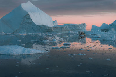 Iceberg in sea against cloudy sky during sunset