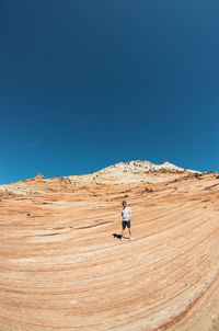 Full length of man walking on desert against clear blue sky