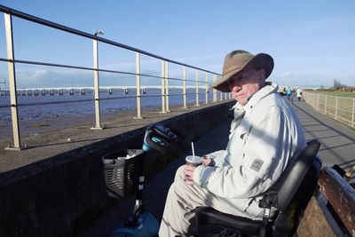 Man sitting on railing by sea against sky