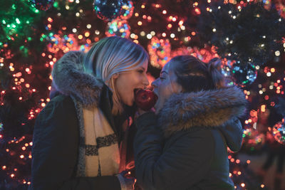 Female friends eating caramelized apple during christmas at night