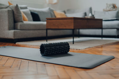 Sturdy black foam roller on a fitness mat, modern interior, selective shallow focus.
