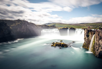 Scenic view of waterfall against cloudy sky