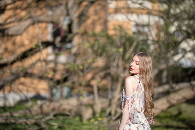 Beautiful young woman standing against trees in park