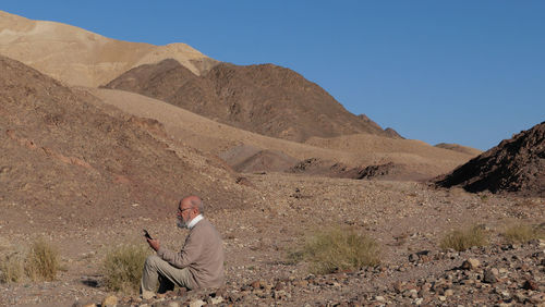 Senior man sitting in the desert with smart phone 