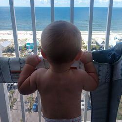 Rear view of shirtless boy looking at sea