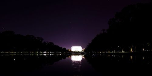 Silhouette trees by lake against sky at night