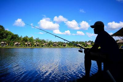 Man fishing in water against blue sky