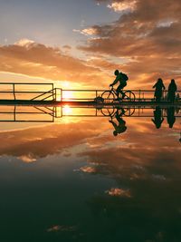 Silhouette people sitting by lake against sky during sunset