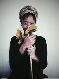 Portrait of young woman smelling sunflowers against wall