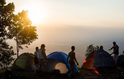 Group of people standing by tents on mountain during sunset