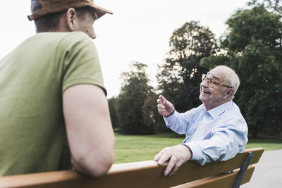 Happy senior man relaxing together with his grandson on a park bench