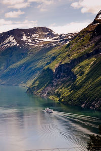 Boat in river by rocky mountains against sky