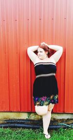 Young woman with hands behind head standing against wall