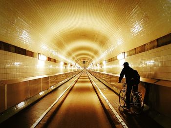 Rear view of woman walking in illuminated tunnel