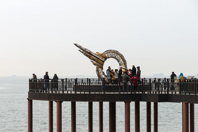 People on pier over sea against clear sky