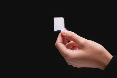 Cropped hand of person holding cigarette against black background