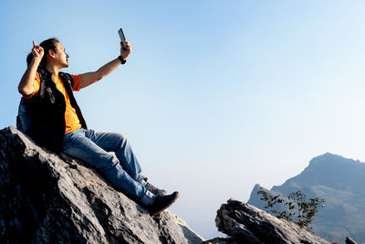 Low angle view of man sitting on rock against sky