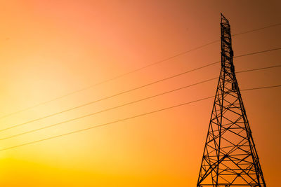 Low angle view of electricity pylon against orange sky