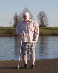 Portrait of woman holding stick while standing by lake against sky