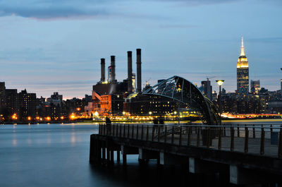 Illuminated bridge over river by buildings against sky at night.