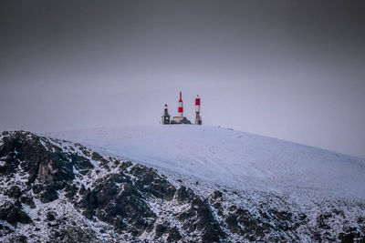 Lighthouse on snowcapped mountain against sky