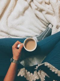 Low section of woman having tea on bed at home