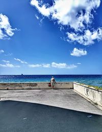 Man on retaining wall by sea against blue sky