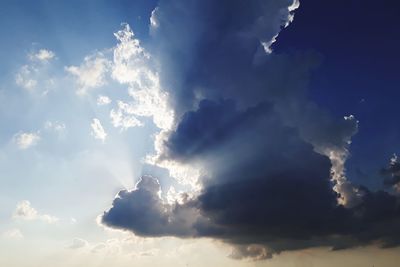 Low angle view of sunlight streaming through clouds