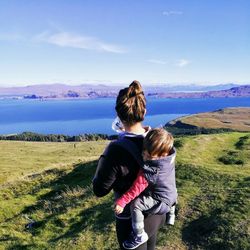 Rear view of siblings standing on lake against sky