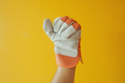 Close-up of hand wearing gloves against yellow background
