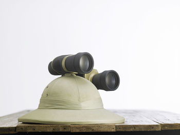 Close-up of hat with binoculars on table against white background