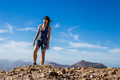 Front view of woman standing on rock against clear blue sky