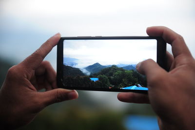 Midsection of person photographing through smart phone against sky