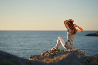 Person on rock at sea against clear sky