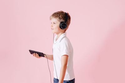 Smiling boy listening music while holding phone against colored background