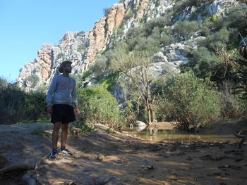 Rear view of woman standing on rock against sky