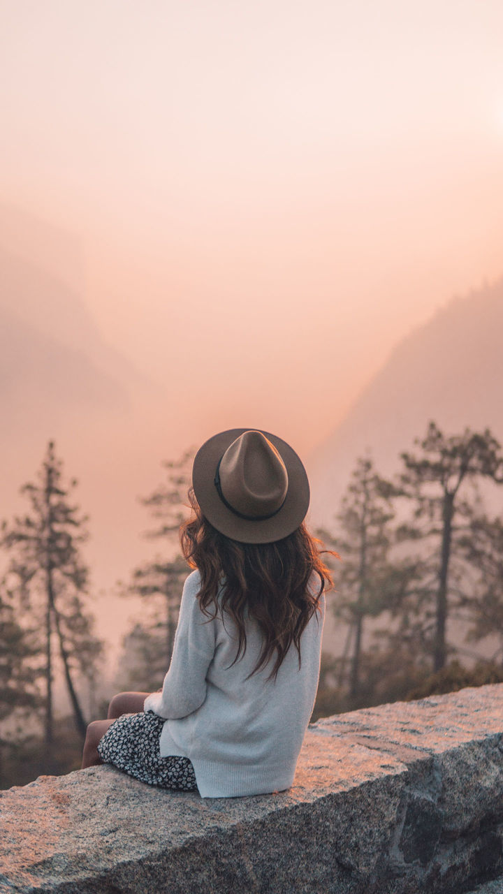 one person, morning, nature, adult, hat, sky, clothing, tree, women, sitting, beauty in nature, sun hat, tranquility, relaxation, tranquil scene, land, sunlight, landscape, mountain, forest, lifestyles, solitude, scenics - nature, leisure activity, environment, copy space, person, plant, vacation, young adult, fog, fashion accessory, zen-like, holiday, trip, female, sun, outdoors, long hair, fedora, idyllic, activity, rock, travel, hairstyle, rural scene, winter, dusk, sunrise, loneliness, non-urban scene, twilight, contemplation, travel destinations, meditating, exercising, spirituality, mountain range, full length