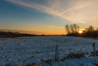 Snow covered field against sky during sunset