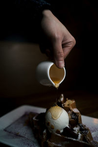 Cropped hand pouring honey over dessert on table