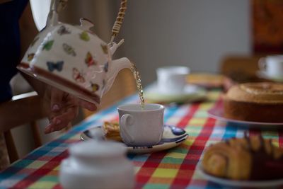 Cropped hand pouring tea in cup on dining table at home