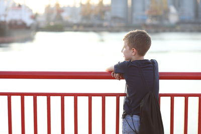 Boy standing by railing against water